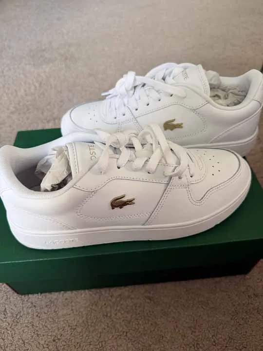 Białe buty Lacoste ze złotym logo na zielonym pudełku